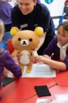School students looking at properties with a stuffed bear in school workshop.