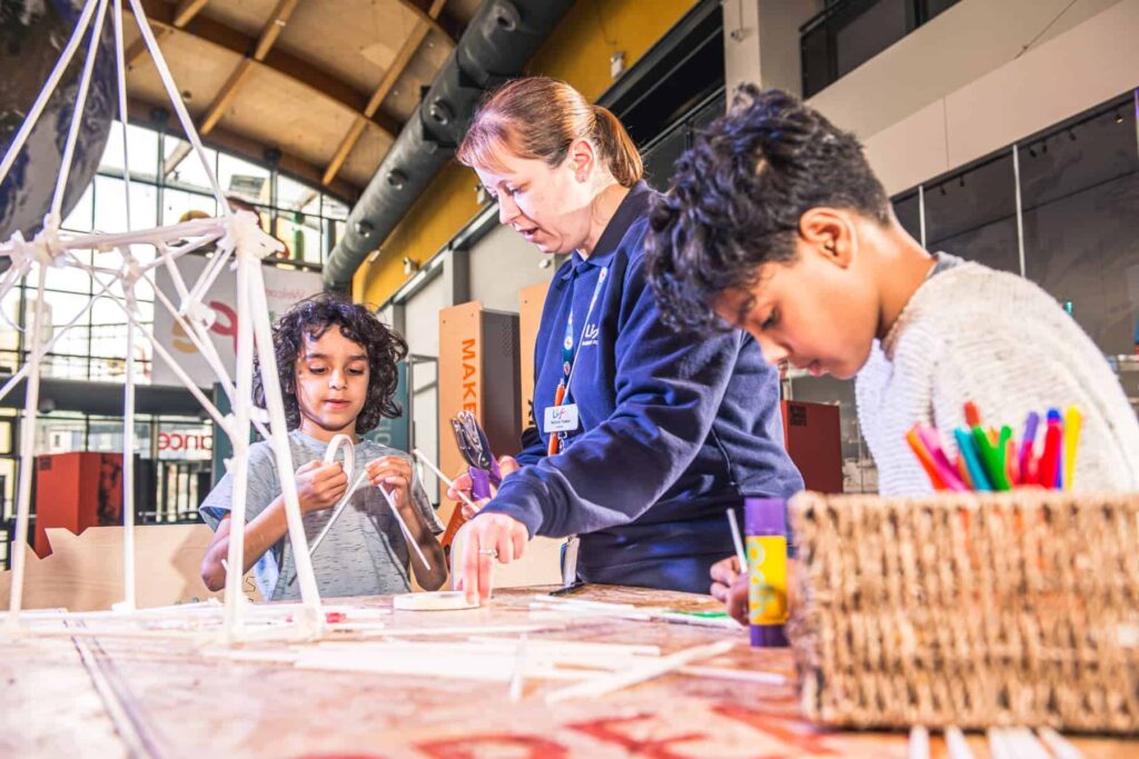 A Life Science Centre Explainer at work in the Making Studios, helping two young visitors with a hands-on activity.