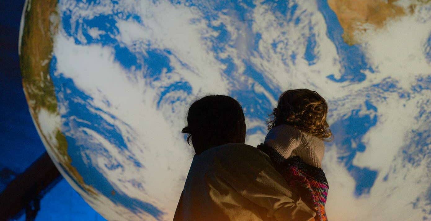 Mother holding small child, looking up at Gaia, Life Science Centre's huge replica of Planet Earth.