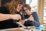 Two female adults gluing a paper craft bird in Life Science Centre's Making Studios.