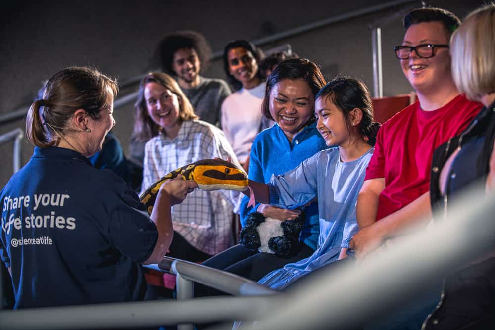 Explainer showing a soft toy snake to audience in Life Science Centre's theatre.