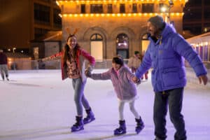 Family of three wrapped up for winter holding hands whilst skatings on Life Science Centre in Newcastle's outdoor ice rink.