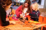 Two children with the assistance of Explainer enjoying a festive craft making activity inside the science centre.