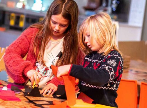 Two children with the assistance of Explainer enjoying a festive craft making activity inside the science centre.