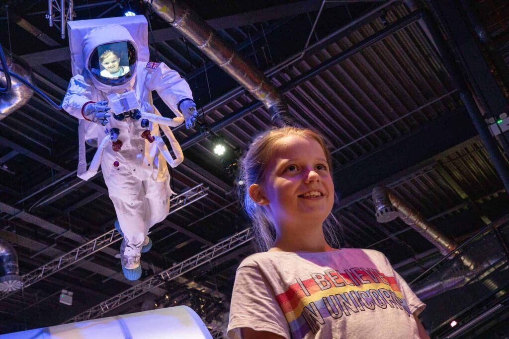 Girl Stood Underneath Astronaut Model With Her Face Projected Onto The Screen.