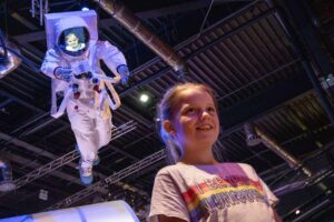 Girl Stood Underneath Astronaut Model With Her Face Projected Onto The Screen.
