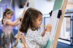 Young Girl Using Easel In Hello World.