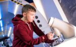 Male teenage visitor wearing a red hoody looking through a microscope in Life's Space Zone.
