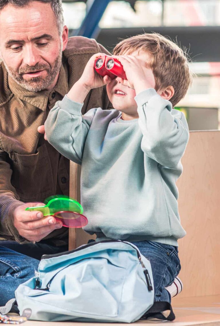 Little Boy Looking Through Red Binoculars Which Are Included In Life Science Centre's Discovery Backpacks.