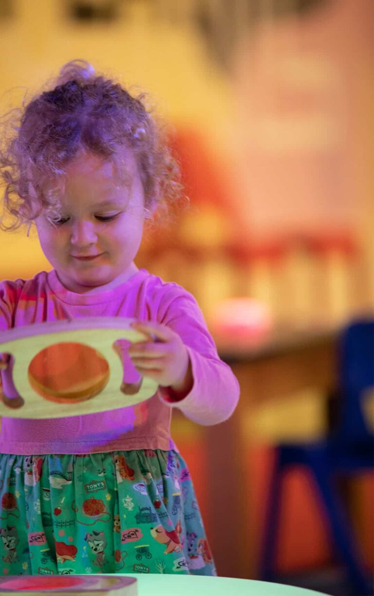 Little girl looking through coloured glass in Play Zone.