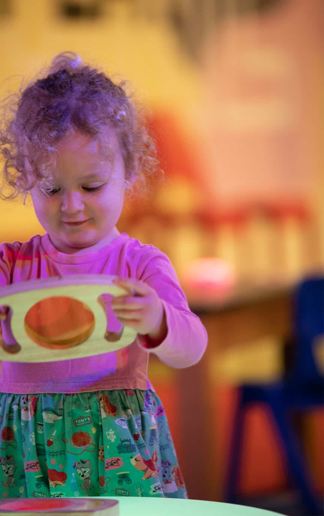 Little girl looking through coloured glass in Play Zone.