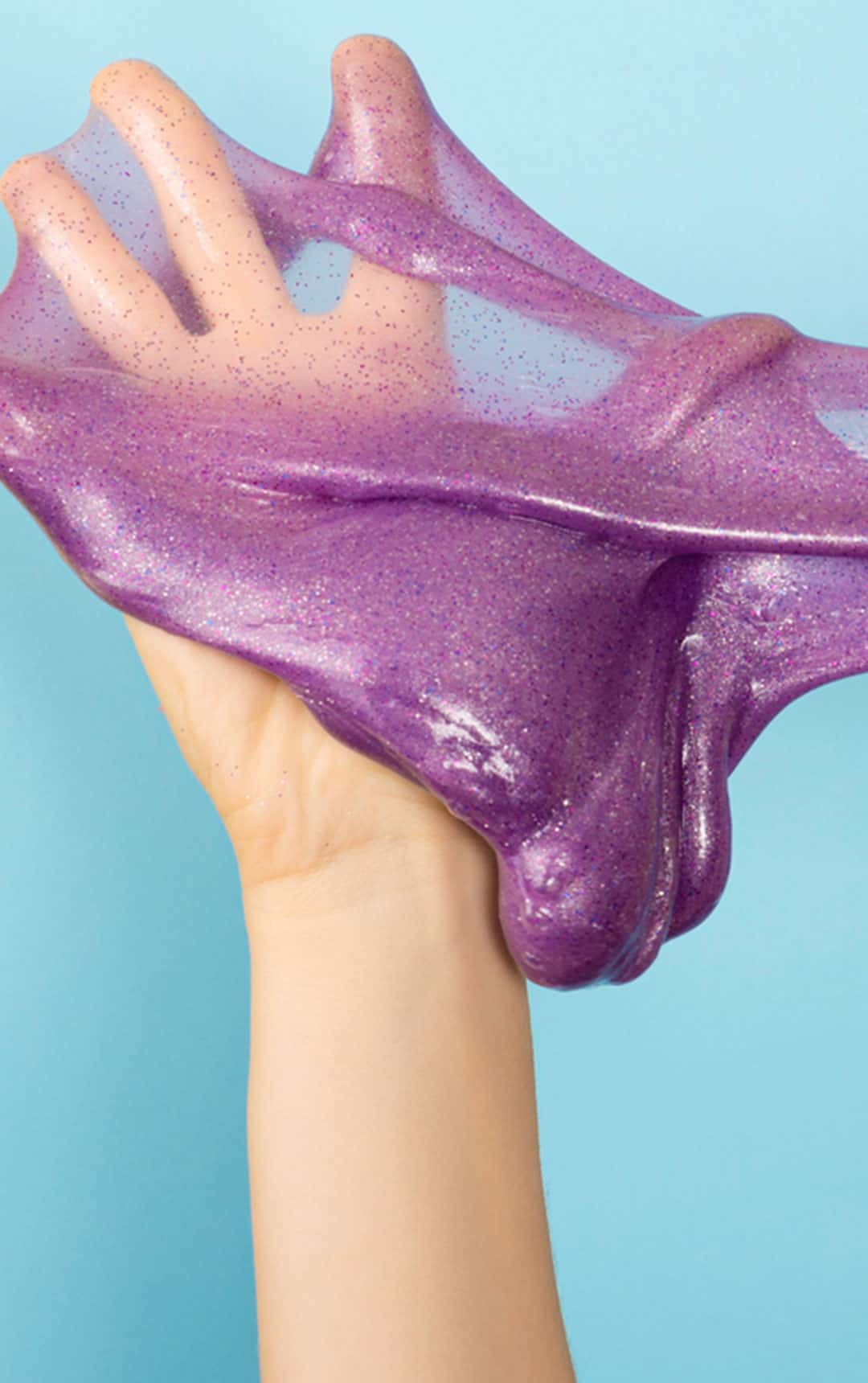 Child's hand covered in a pink, sparkly slime.