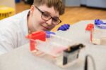 Male student with glasses looking closely at equipment required to complete a PCR experiment in Life Science Centre schools' workshop.