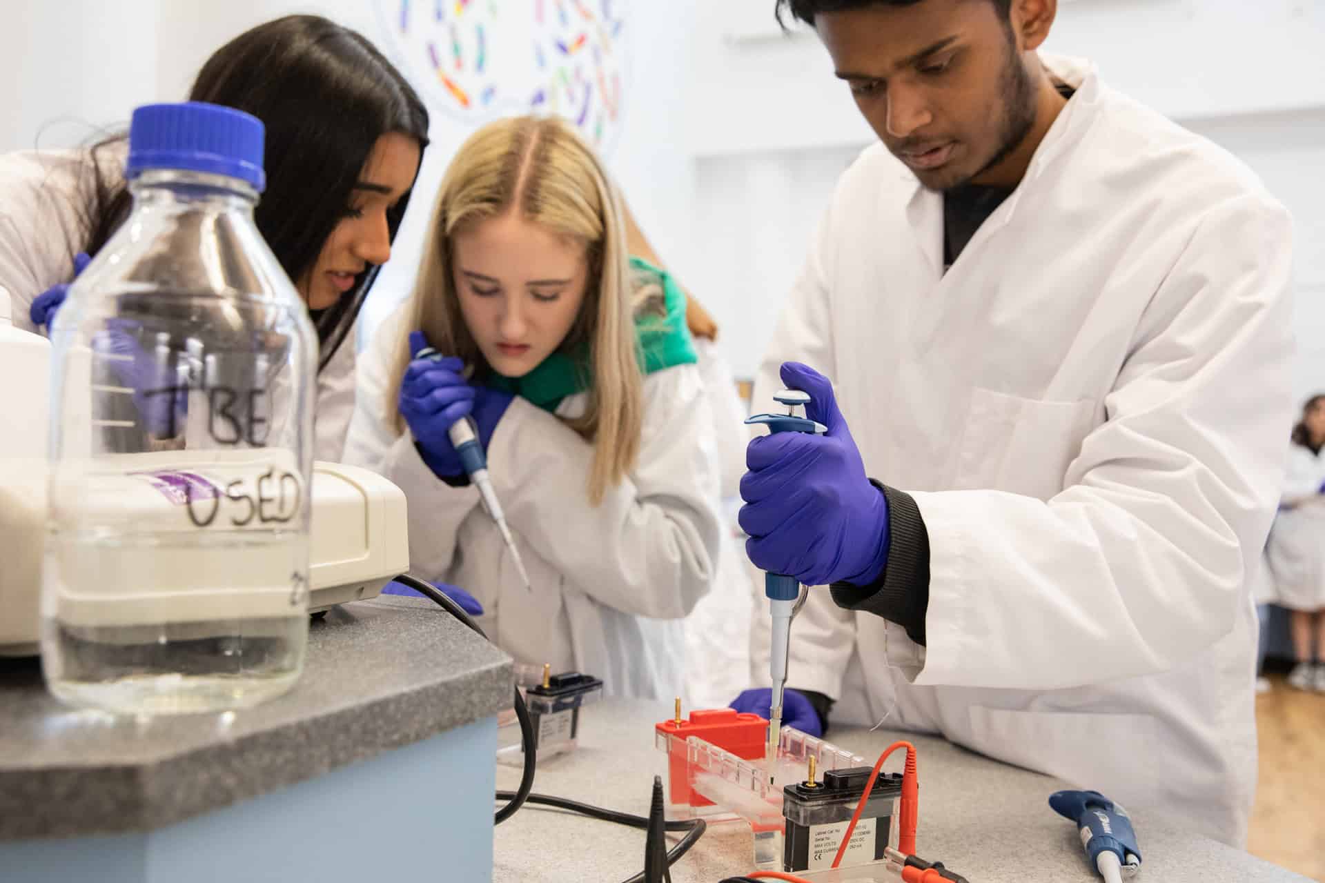 School teenagers in white lab jackets using science equipment during PCR workshop at Newcastle's Life Science Centre.