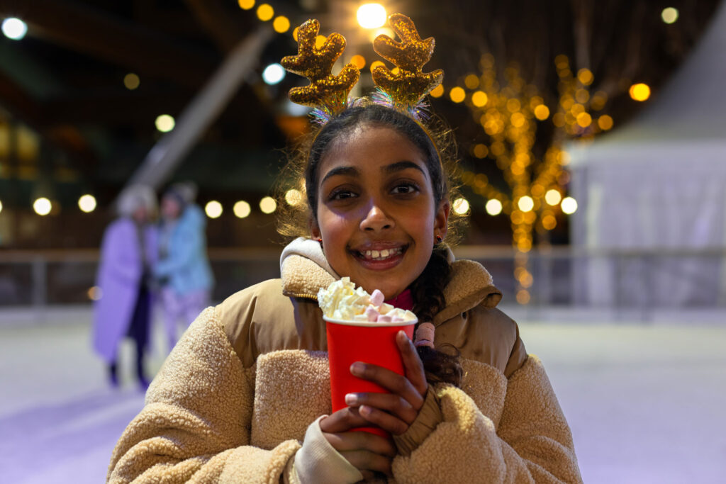 Young girl wearing reindeer antlers enjoying a festive hot chocolate on Life Science Centre's ice rink located in Newcastle.