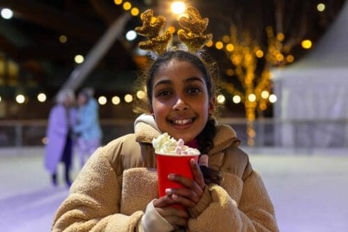 Young girl wearing reindeer antlers enjoying a festive hot chocolate on Life Science Centre's ice rink located in Newcastle.