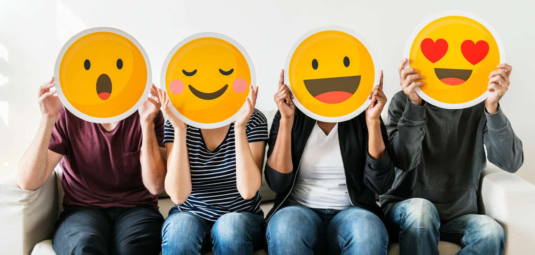 People holding emoji masks to express emotion through technology on sofa white background