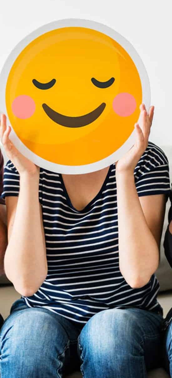 People holding emoji masks to express emotion through technology on sofa white background