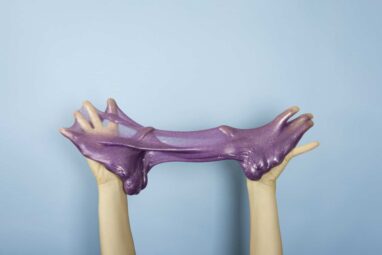 Close up on shiny purple or violet slime in the hand isolated on blue background. fun and stress relief concept.