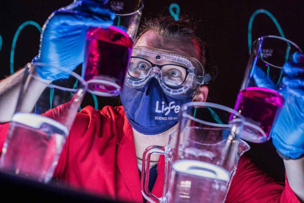 Explainer looking closely at beakers of colured chemicals in Science Theatre