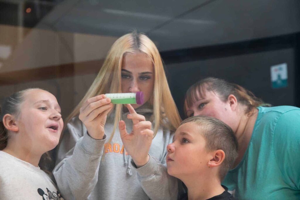 A family of four looking through at test tube at bright green liquid in Life Science Centre's Experiment Zone.