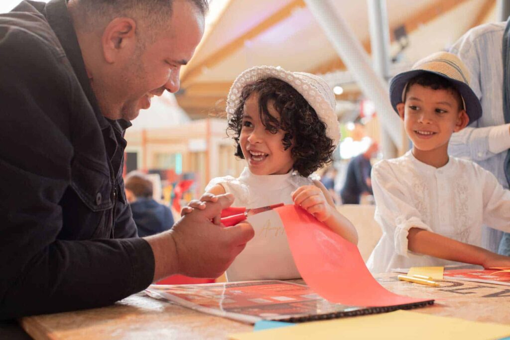 Father with son and daughter in Making Studios completing a craft activity together in summer clothing.
