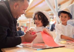 Father with son and daughter in Making Studios completing a craft activity together in summer clothing.