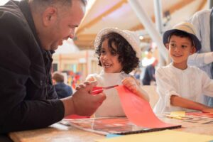 Father with son and daughter in Making Studios completing a craft activity together in summer clothing.