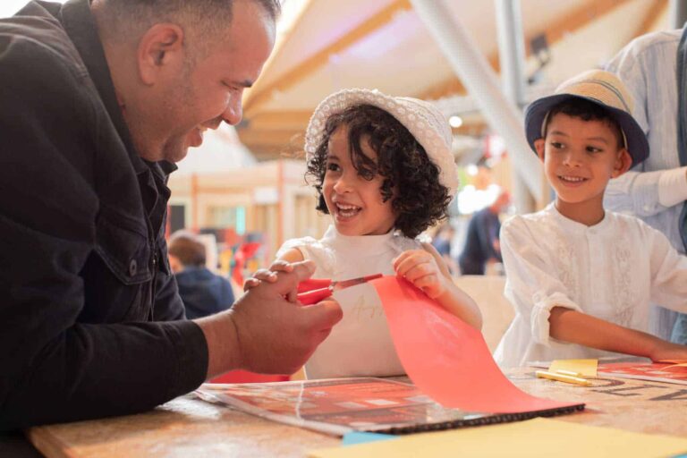 Father with son and daughter in Making Studios completing a craft activity together in summer clothing.