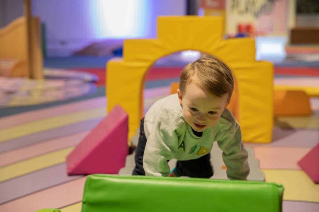 Toddler climbing in soft play area inside science centre.