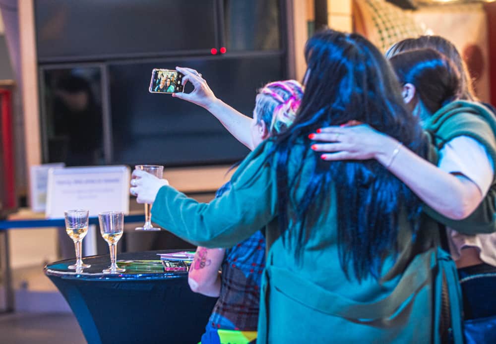 Adults enjoying a drink whilst taking a selfie at an evening event inside the science centre.