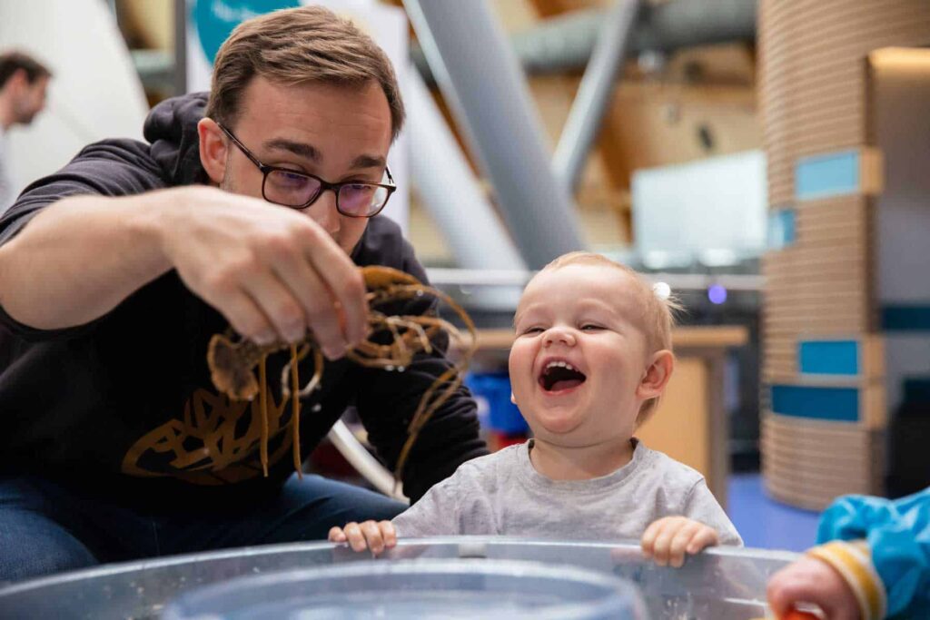 Father And Toddler Enjoying Water Play At Pre School Day.