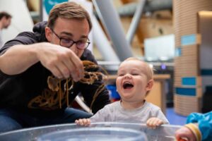 Father And Toddler Enjoying Water Play At Pre School Day.