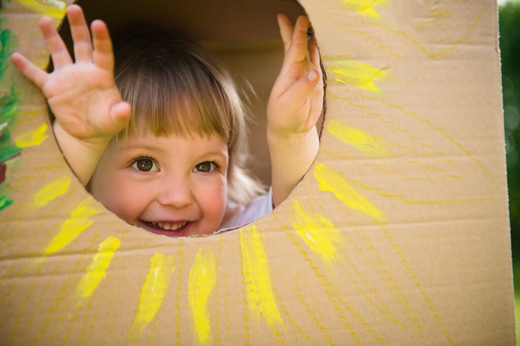 Little child looking through window of children's house made of big box.