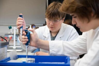 Two male students in white lab coats using pipettes in Forensic DNA workshop.