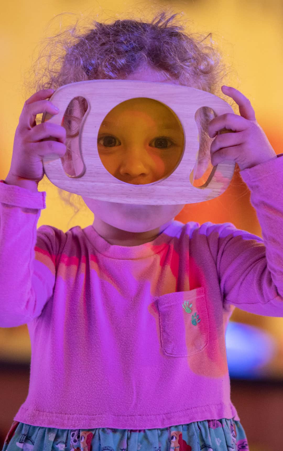 Little girl looking through coloured glass in Play Zone.