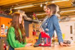 Lead Maker Molly in Life Science Centre's Making Studios assisting a young female visitor with a hands-on bage making activity.