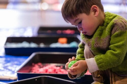 Little boy in green jumper playing with clay at Life Science Centre Pre-School Day.