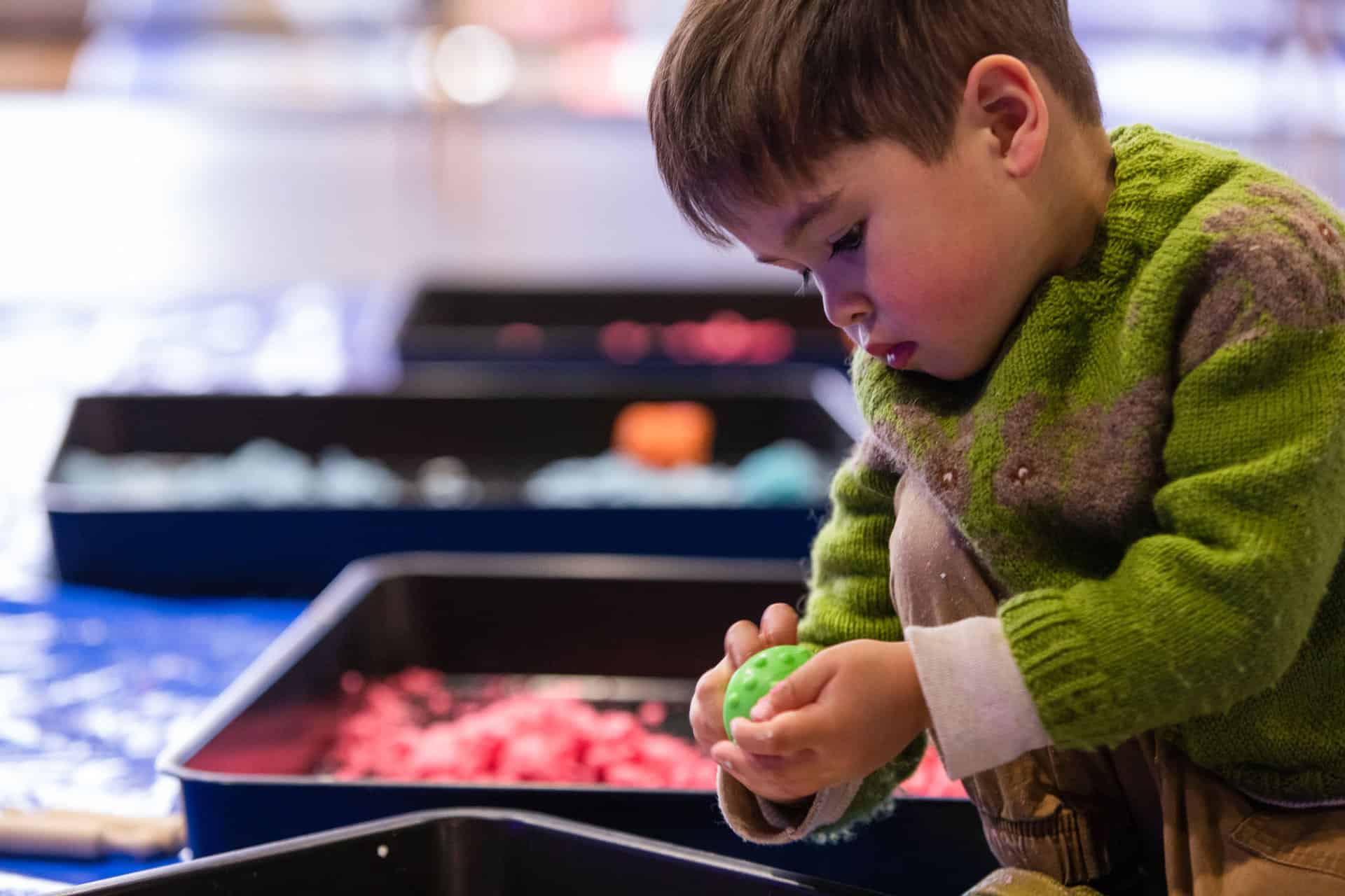 Little boy in green jumper playing with clay at Life Science Centre Pre-School Day.