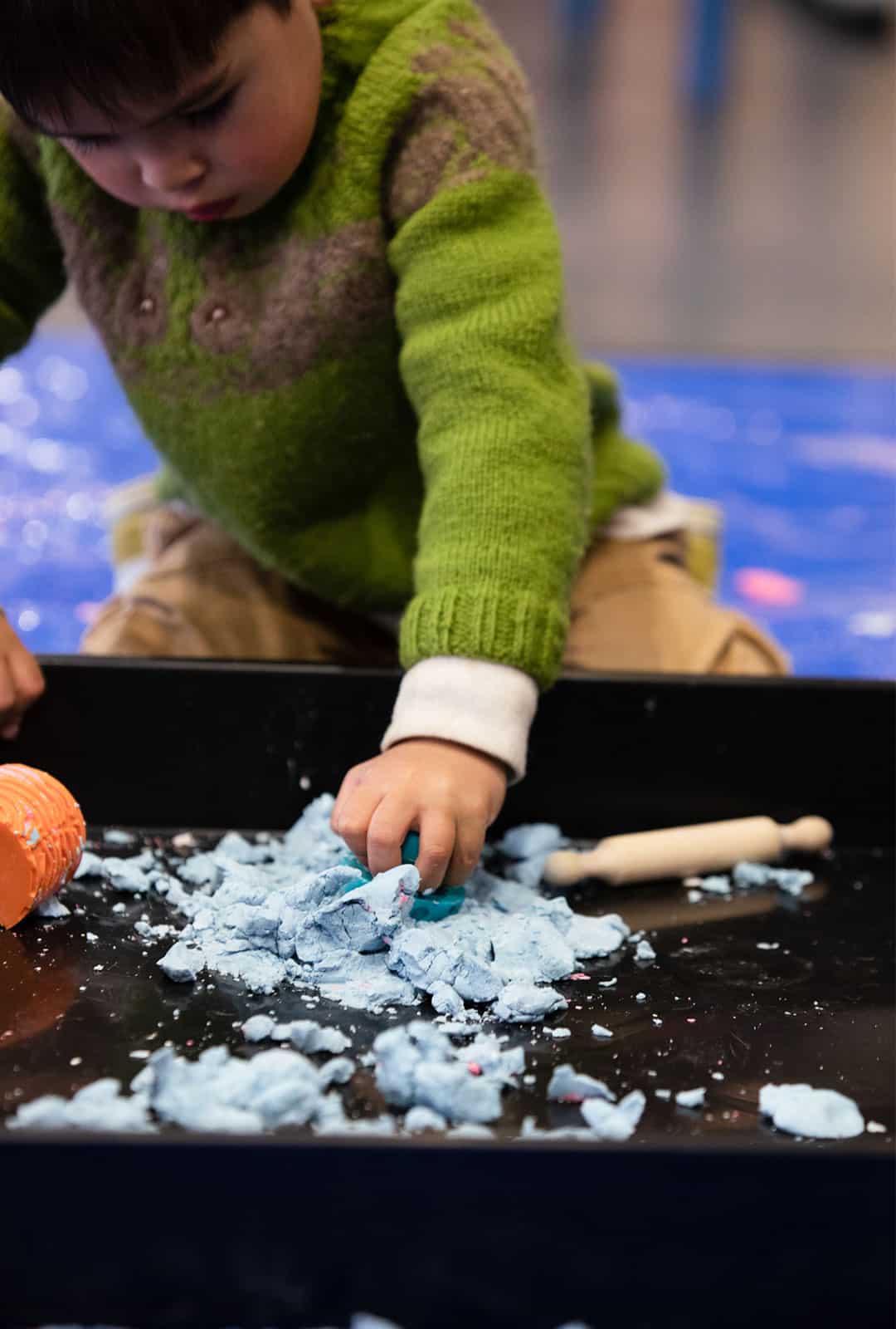 Little boy in green jumper playing with clay at Life Science Centre Pre-School Day.