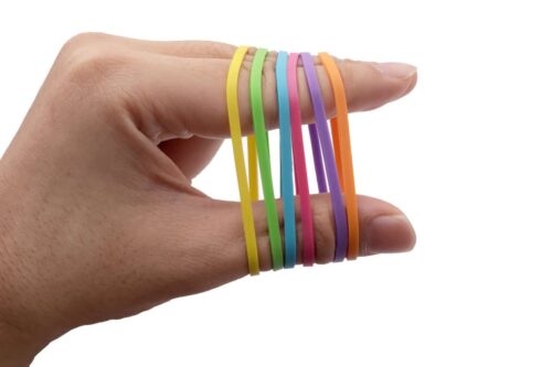 Close Up Of Person Hand Pulling Colorful Multi Color Rubber Bands Around His Fingers, Isolated On White