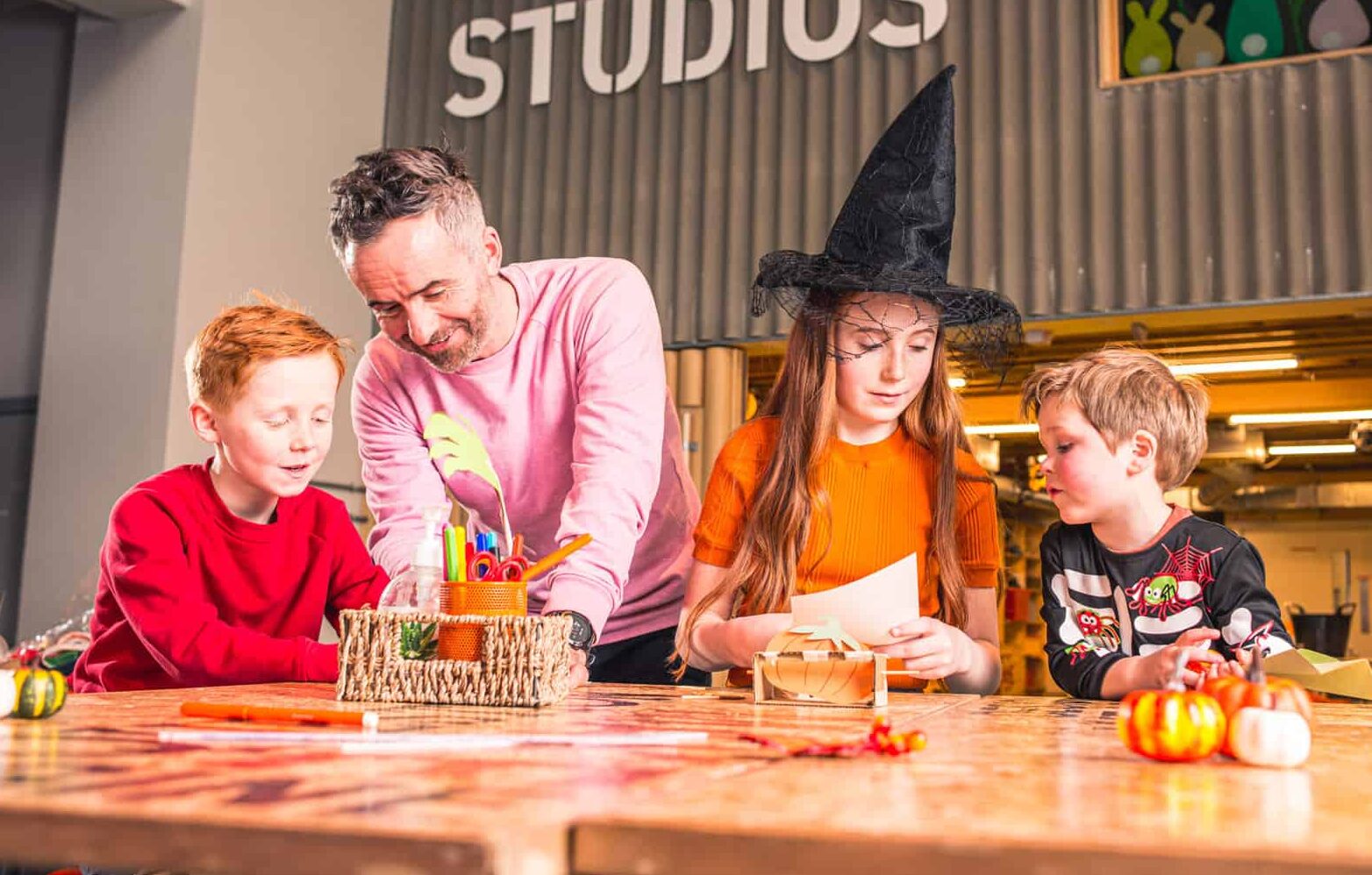 Family sat in Life Science Centre's Making Studio. Girl is in spooky hat completing halloween themed activity.