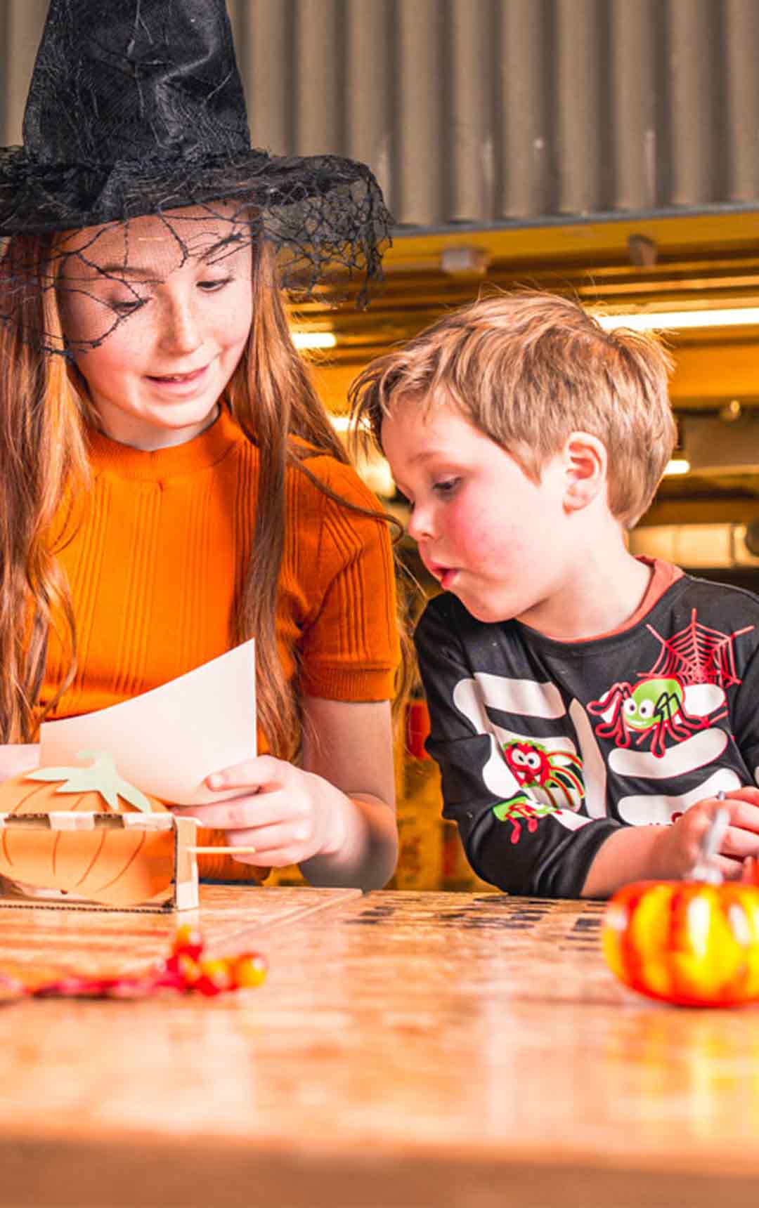 Family sat in Life Science Centre's Making Studio. Girl is in spooky hat completing halloween themed activity.