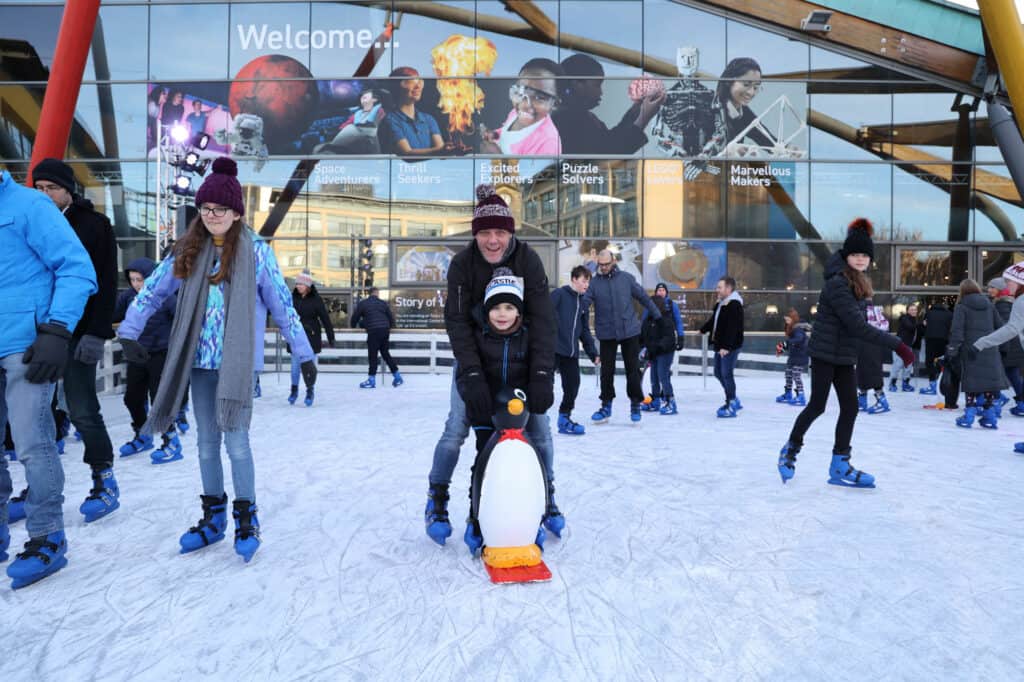 Father and son on Life's outdoor ice rink using penguin skating aid.