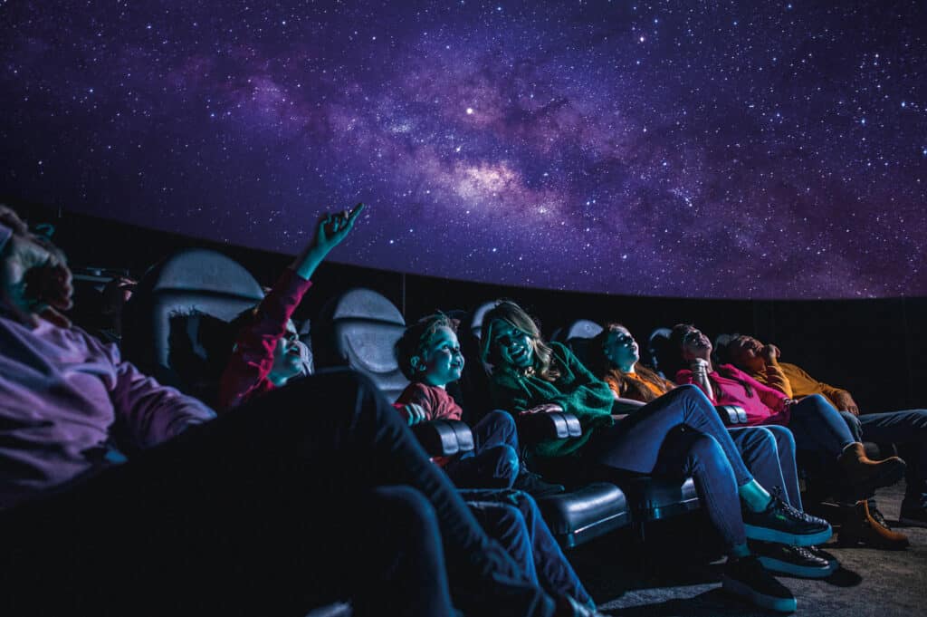 Family of all ages in Life science centre's planetarium watching a 'Just Look Up'.