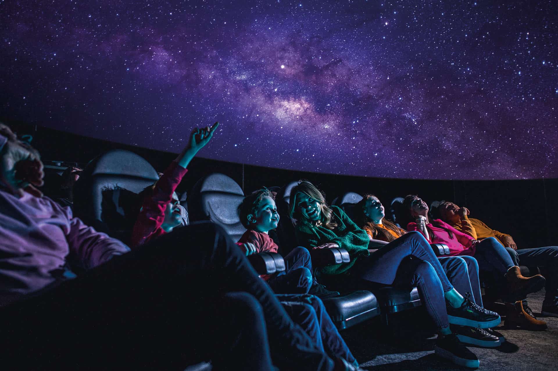 Family of all ages in Life science centre's planetarium watching a 'Just Look Up'.