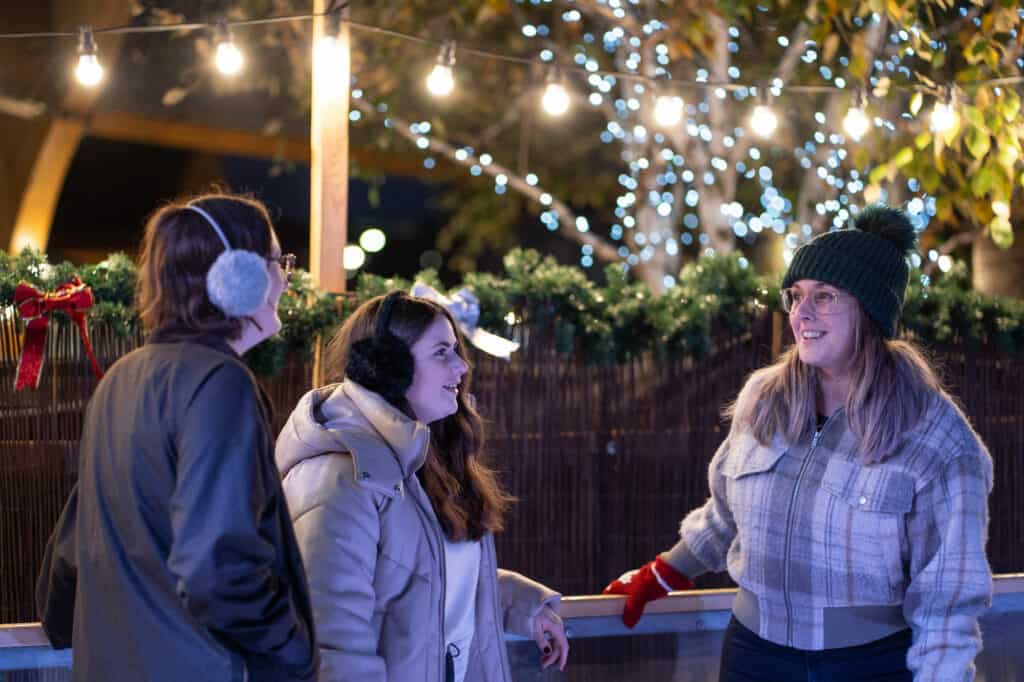 Three women on ice rink in winter clothing laughing and talking.