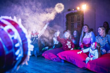 Santa and elf with children receiving a Christmas gift in his Grotto at Newcastle's Life Science Centre.
