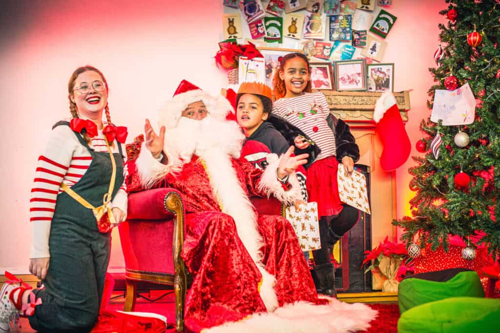 Santa and elf with children receiving a Christmas gift in his Grotto at Newcastle's Life Science Centre.