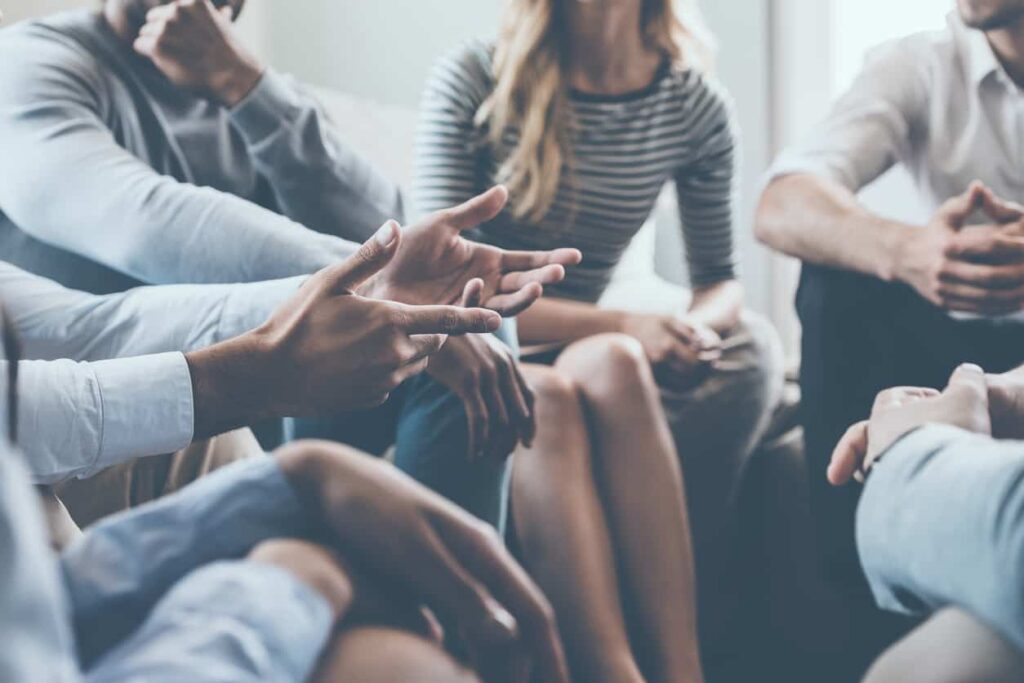 Close-up of people communicating while sitting in circle and gesturing.